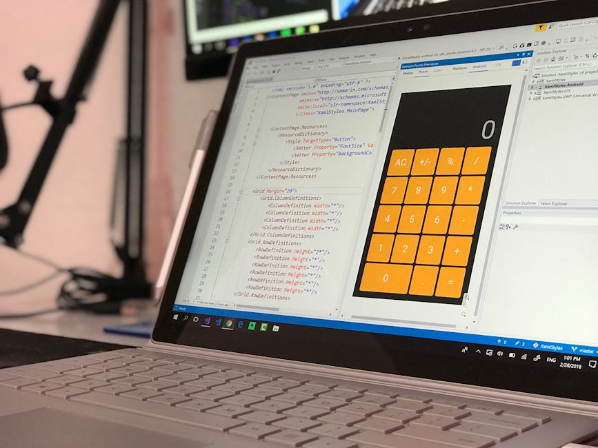 The image shows a laptop computer placed on a desk, displaying a screen with lines of code in HTML and CSS on the left side and a digital calculator interface with large orange buttons on the right si